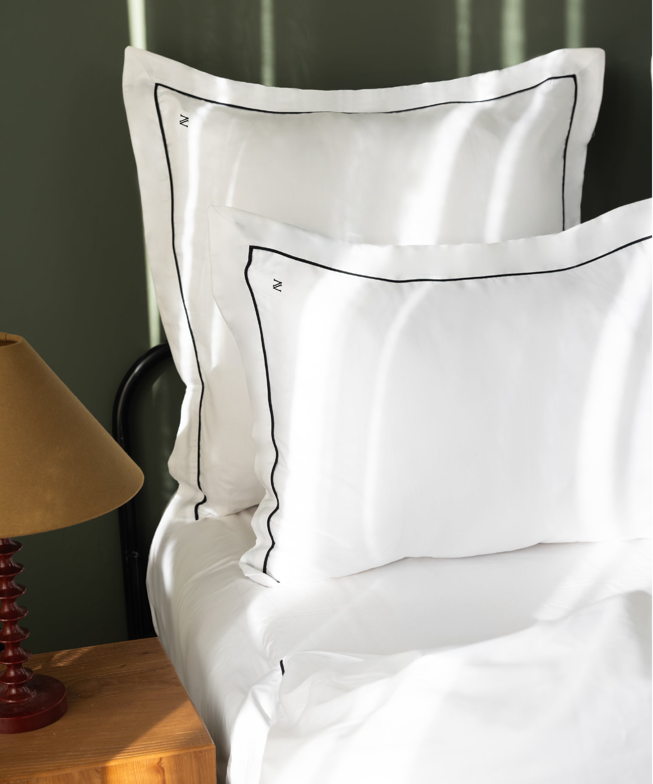 Close-up of luxury sateen Oxford pillowcases showing fine black contrast piping and monogram embroidery – Limasso London