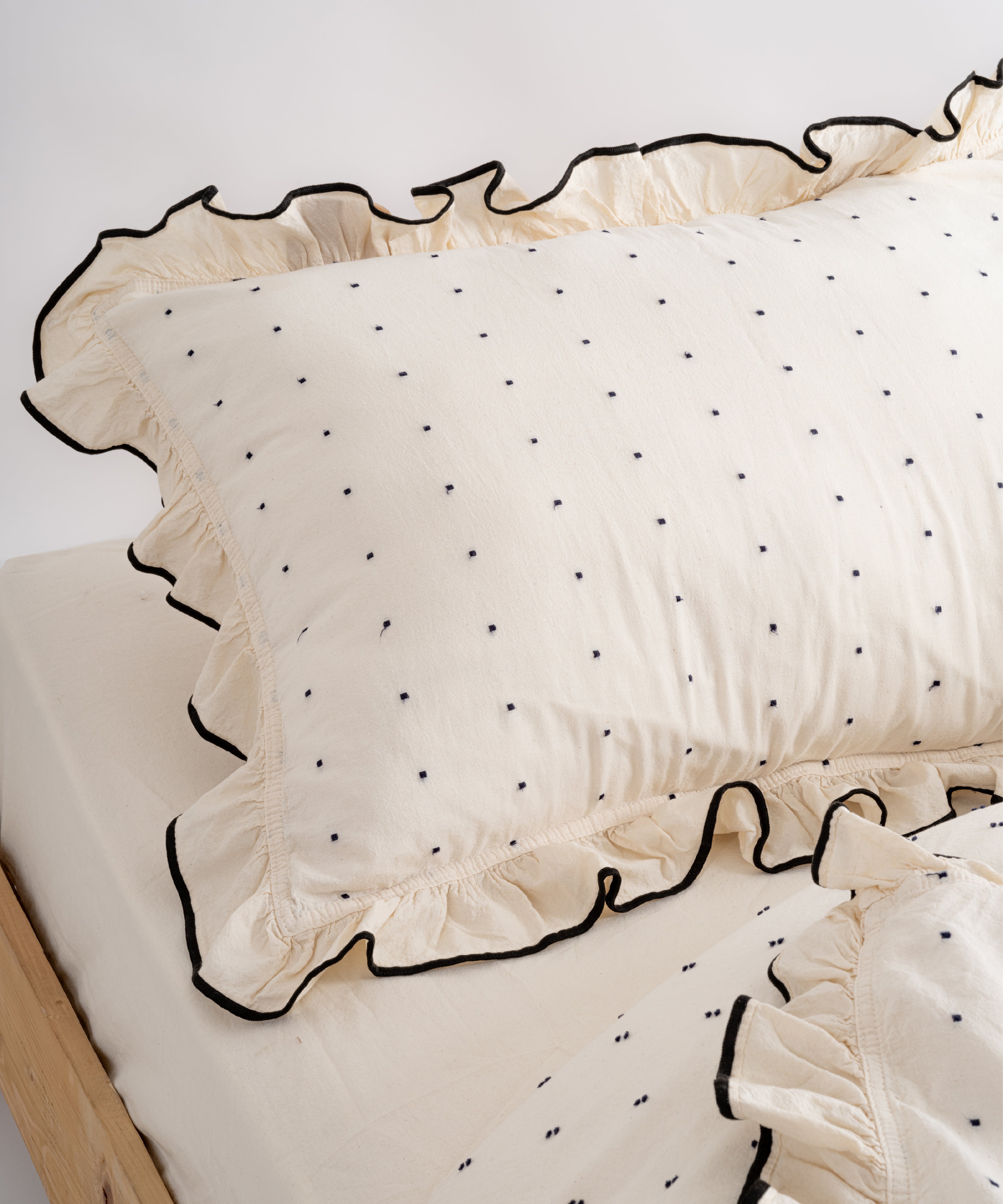 Close-up of Limasso London garment-washed cotton pillowcase with black micro-dot embroidery and embroidered ruffle trim – natural cream colour