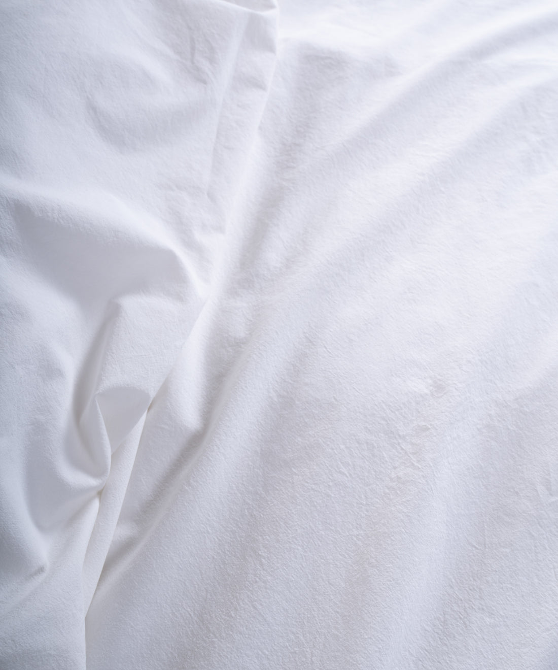 Soft stonewashed white cotton fitted sheet styled on modern bedroom bed, breathable natural cotton bedding for all seasons.