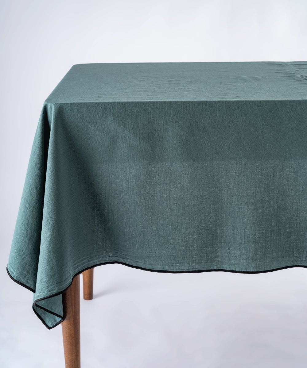 Dark green stonewashed 100% cotton tablecloth with embroidered edges on rectangular dining table, soft textured fabric table linen for modern UK homes