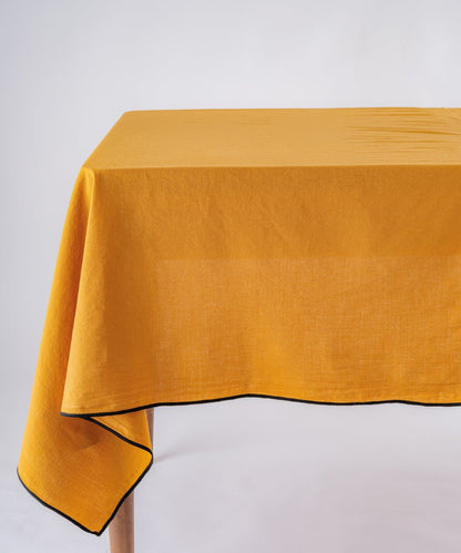 Mustard stonewashed 100% cotton tablecloth with embroidered edges on rectangular dining table, soft textured dining table linen for UK homes