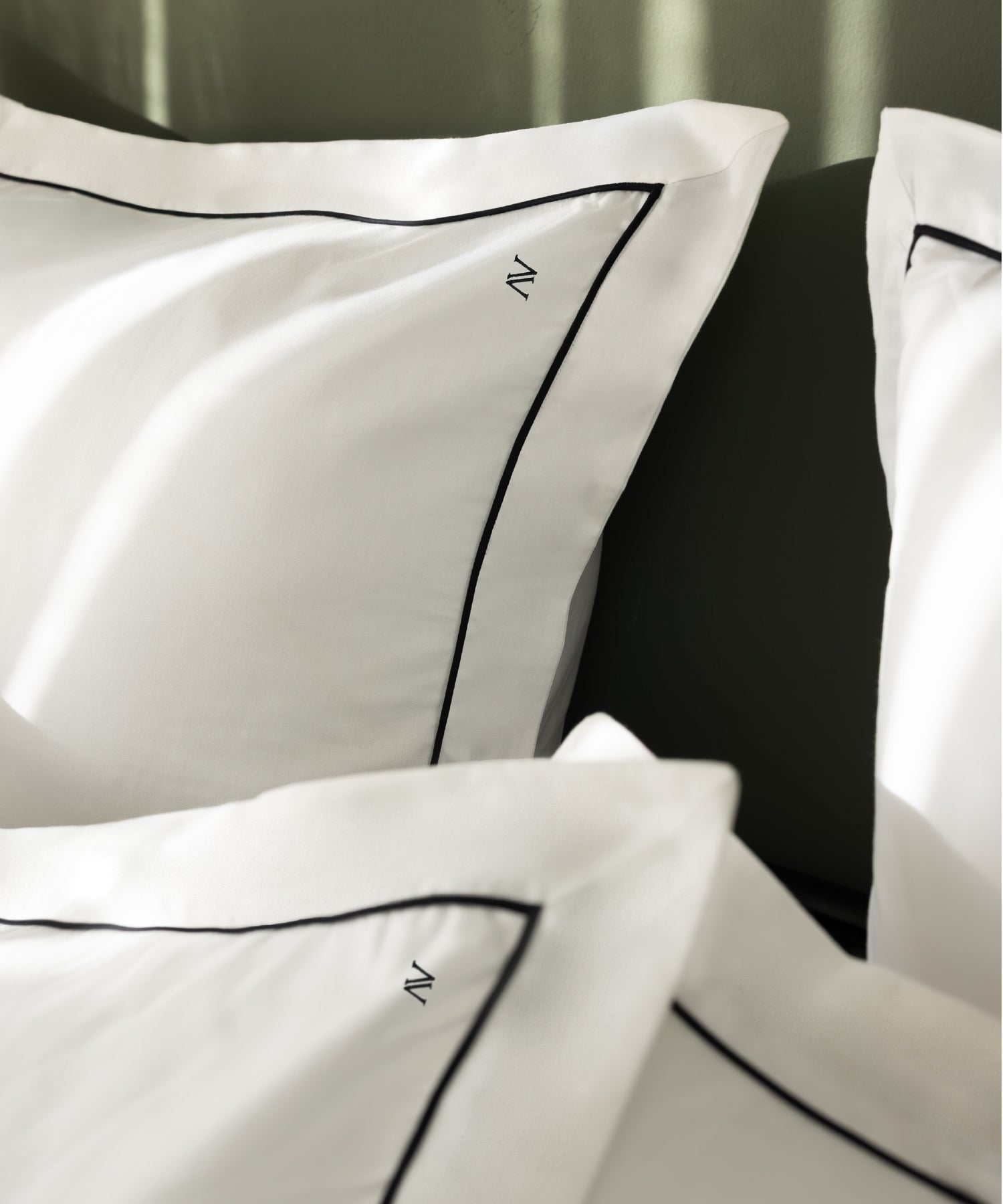 Macro close-up of luxury sateen Oxford pillowcases showing fine black contrast piping and N monogram detail – Limasso London