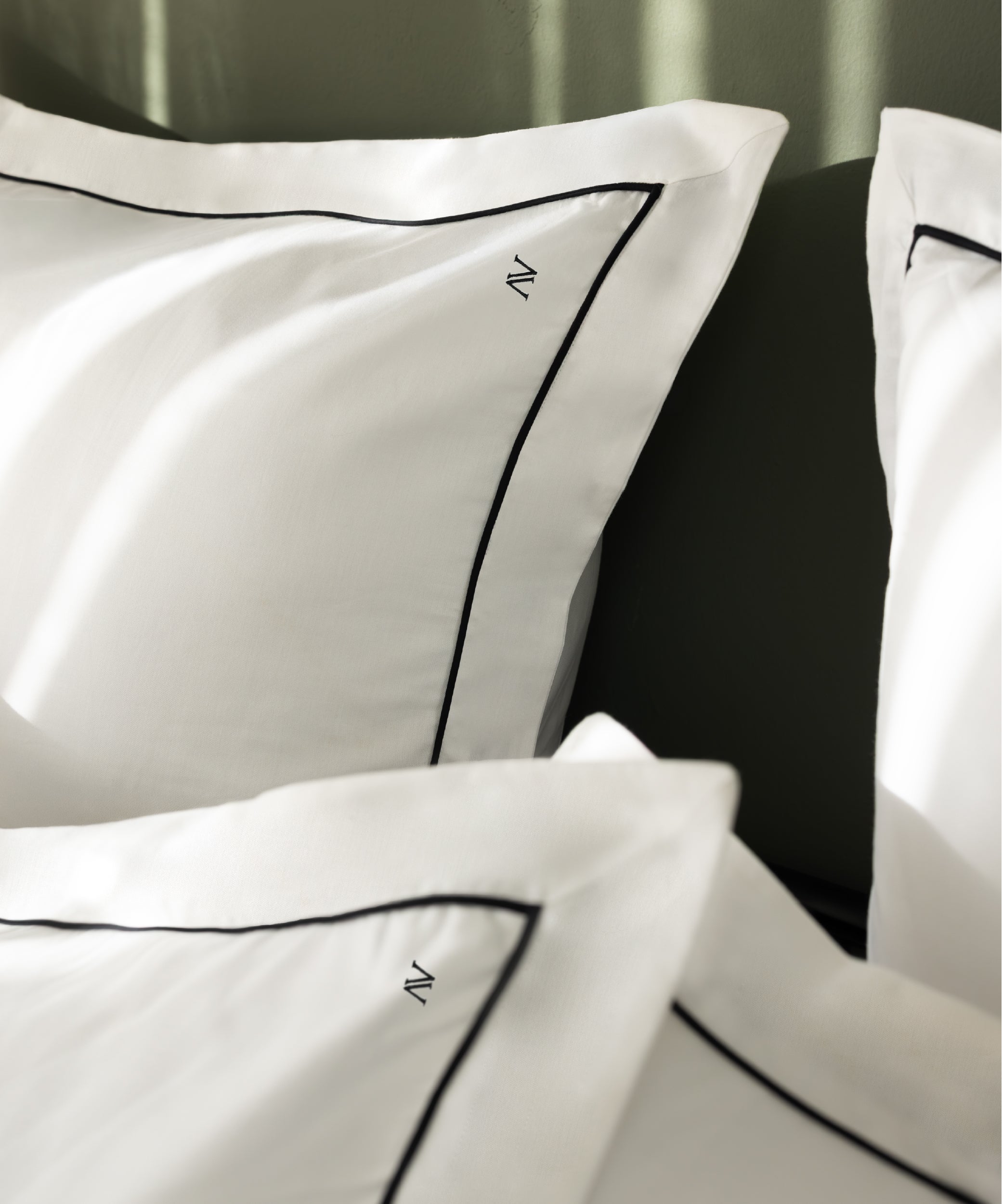 Macro close-up of luxury sateen Oxford pillowcases showing fine black contrast piping and N monogram detail – Limasso London