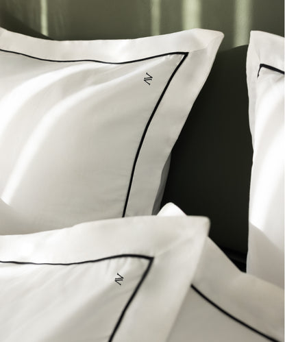 Macro close-up of luxury sateen Oxford pillowcases showing fine black contrast piping and N monogram detail – Limasso London