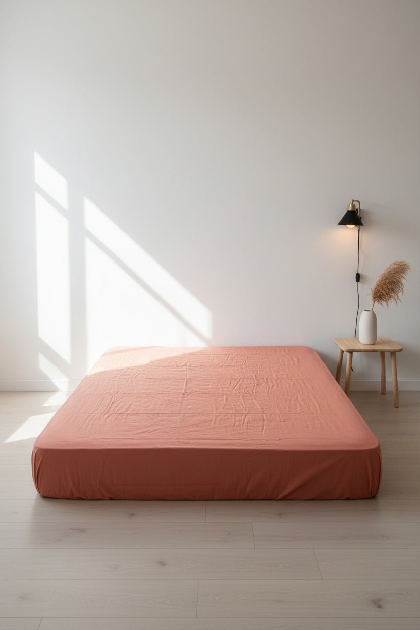 Mecca Orange stonewashed cotton fitted sheet styled on a bed, showing warm terracotta tone, soft texture and secure fitted design.