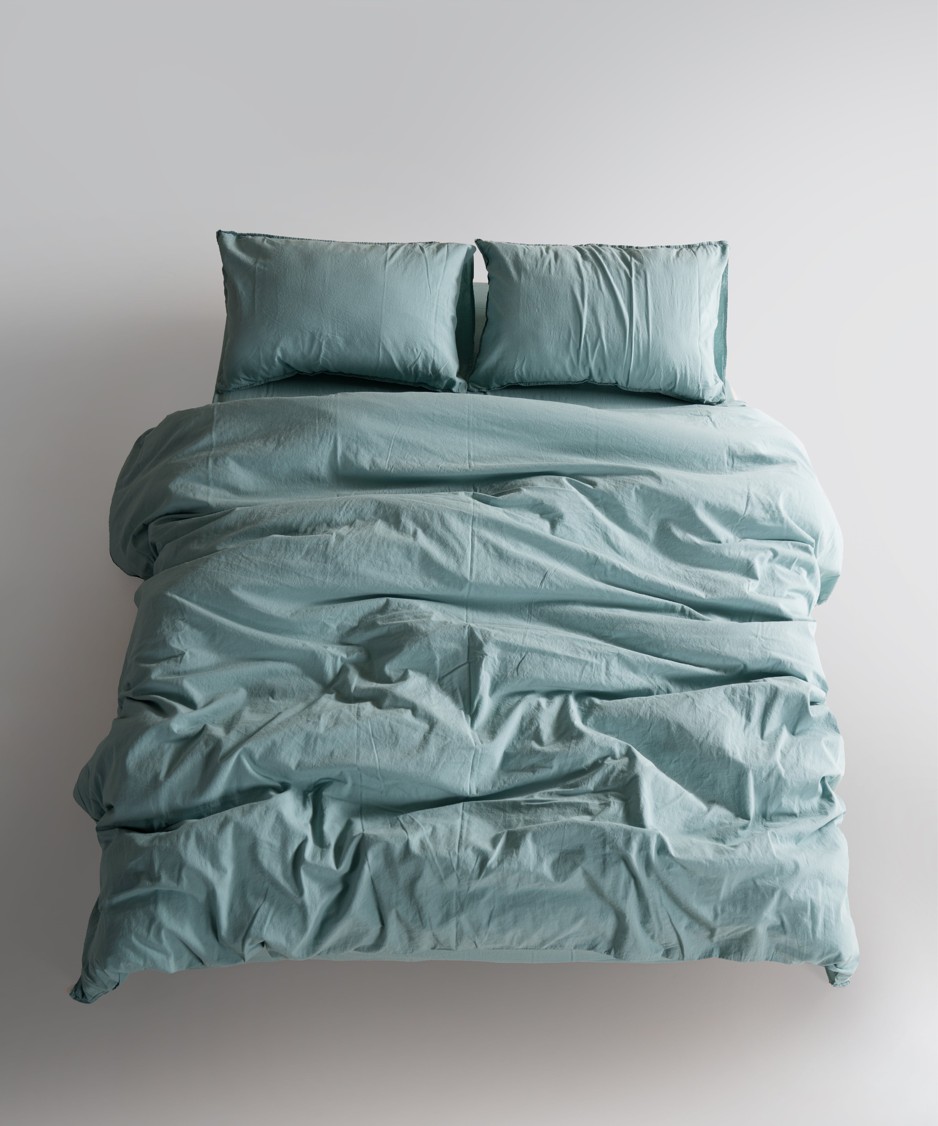 Mineral Blue cotton pillowcase styled on bed. Stonewashed fabric adds a calm, modern and natural look to your bedroom.