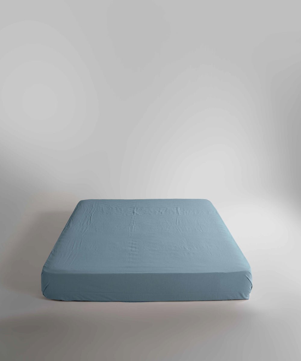 Close-up of a Mineral Blue fitted sheet made from 100% stonewashed cotton. Naturally soft texture, elasticated corners and a secure fit for UK beds up to 40 cm depth.