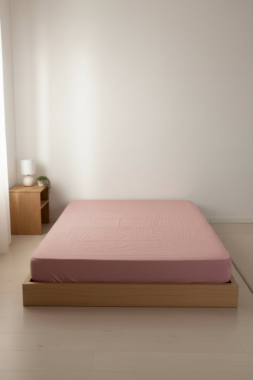 Old Rose stonewashed cotton fitted sheet styled on a bed, showing soft texture, relaxed finish and secure elastic fit on mattress.