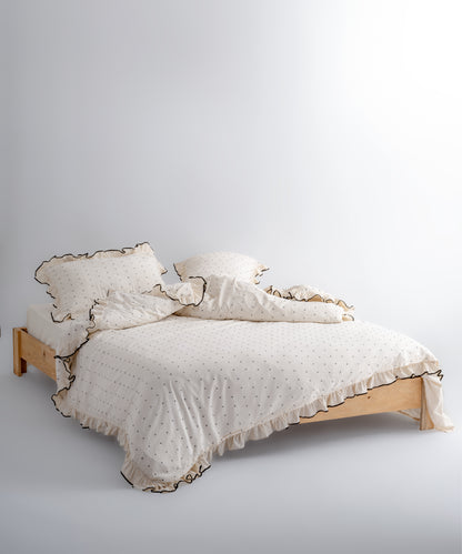 Close-up of Limasso London garment-washed cotton pillowcase with black micro-dot embroidery and embroidered ruffle trim – natural cream colour
