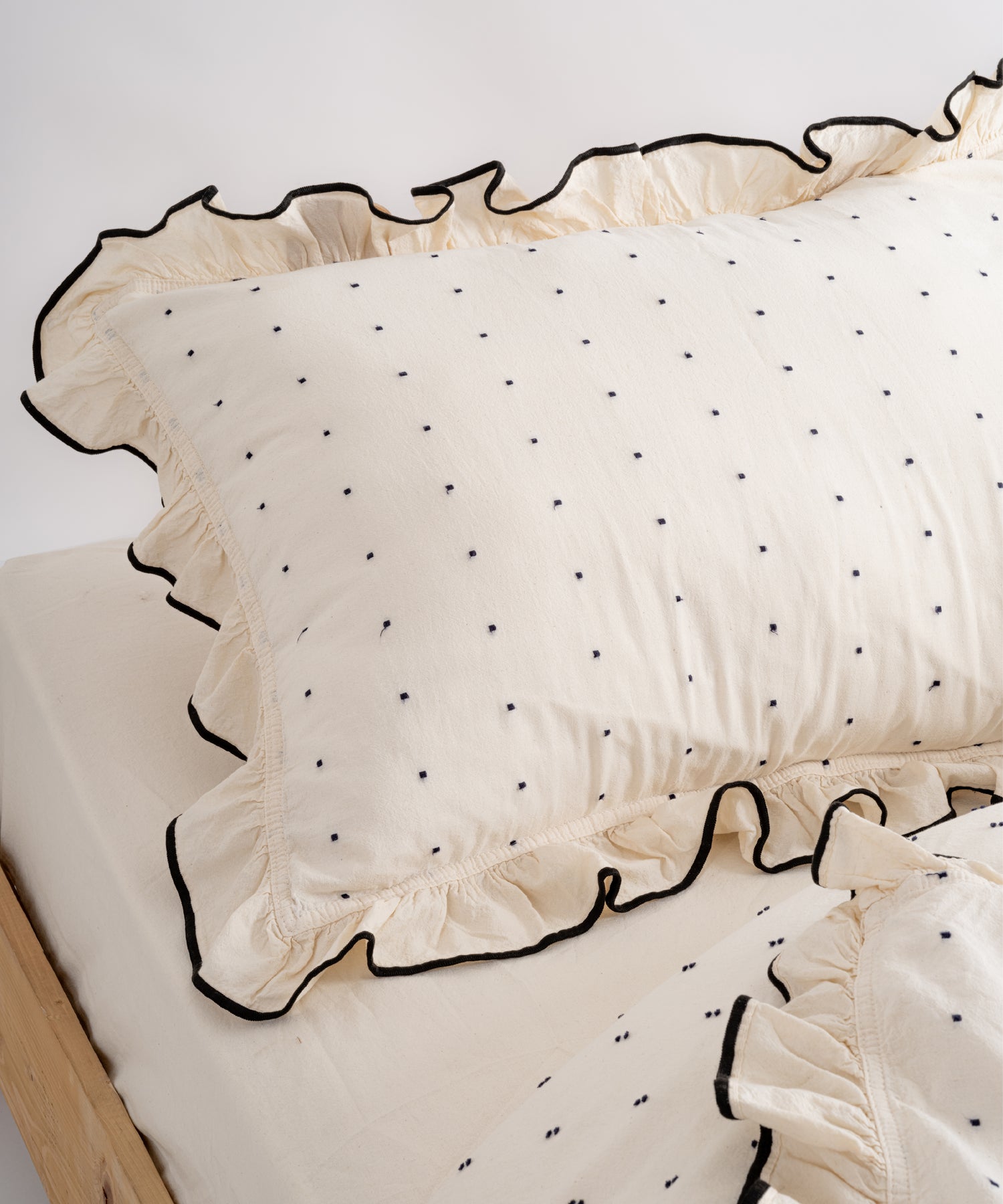 Close-up of Limasso London garment-washed cotton pillowcase with black micro-dot embroidery and embroidered ruffle trim – natural cream colour