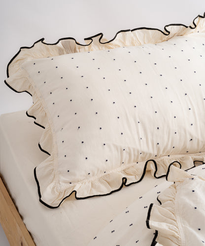Close-up of Limasso London garment-washed cotton pillowcase with black micro-dot embroidery and embroidered ruffle trim – natural cream colour
