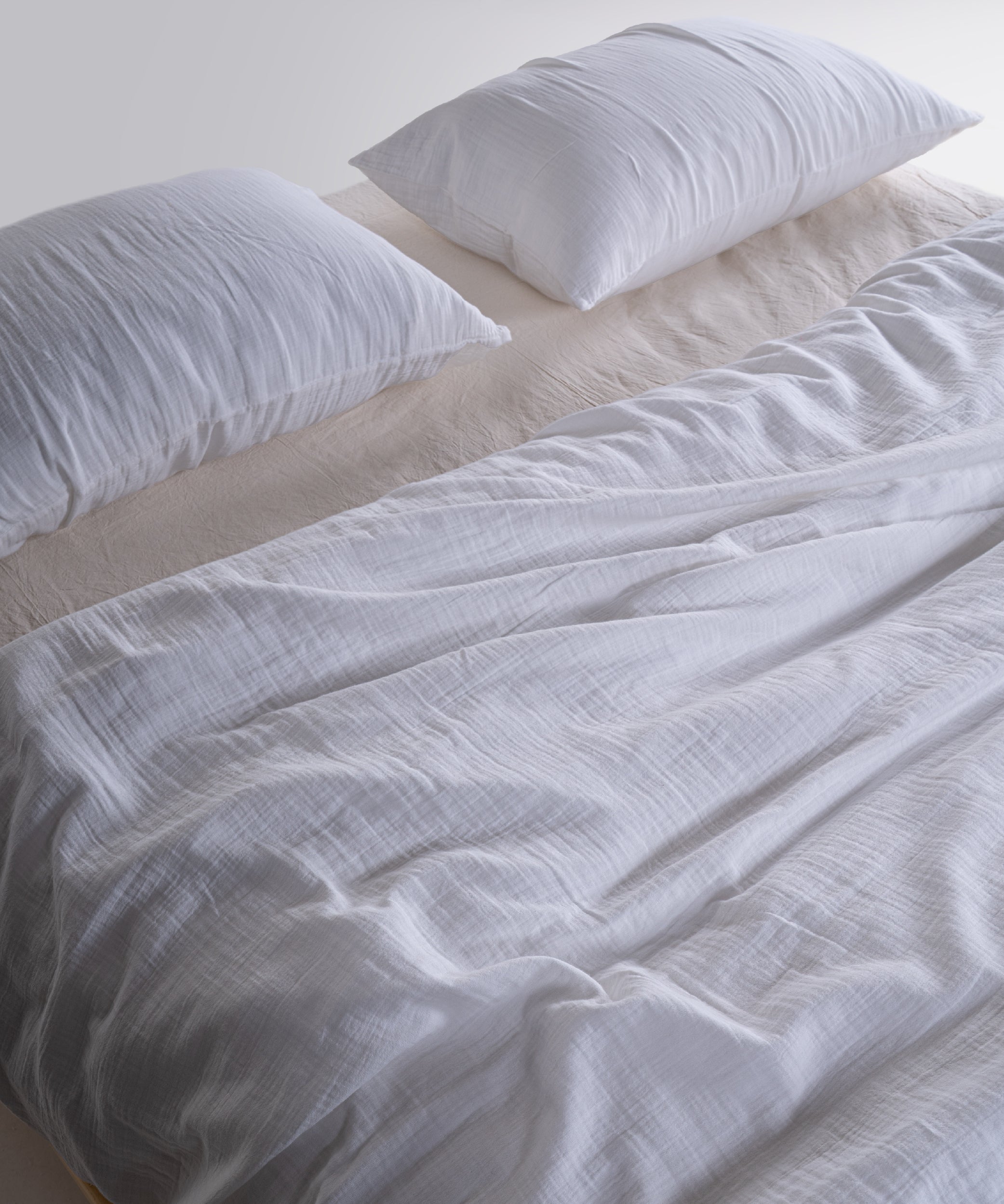 Cloud Muslin Gauze Duvet Cover Set Snow White at 45-degree angle on a low wooden platform bed – Limasso London
