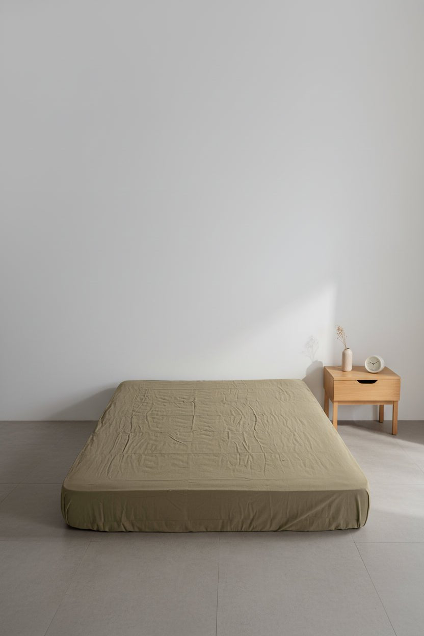 Stonewashed 100% cotton fitted sheet in med green, shown on a minimalist bed setting. Soft, breathable fabric with a relaxed finish, designed to fit UK mattresses perfectly.