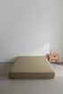 Stonewashed 100% cotton fitted sheet in med green, shown on a minimalist bed setting. Soft, breathable fabric with a relaxed finish, designed to fit UK mattresses perfectly.