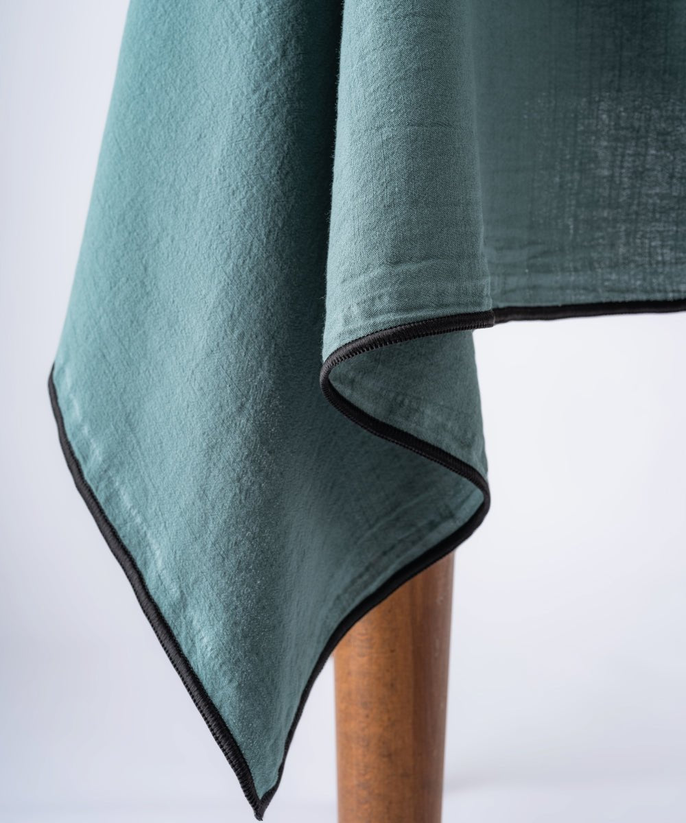 Close up of dark green stonewashed cotton tablecloth showing soft texture and embroidered edge detail, premium dining table linen UK