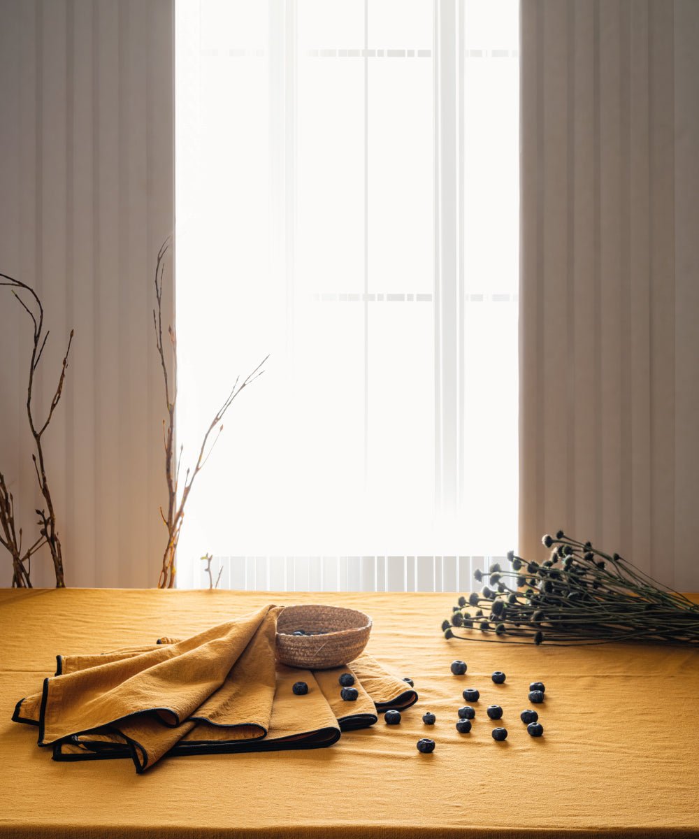 Close up of mustard stonewashed cotton tablecloth showing soft texture and embroidered edging detail, premium UK table linen