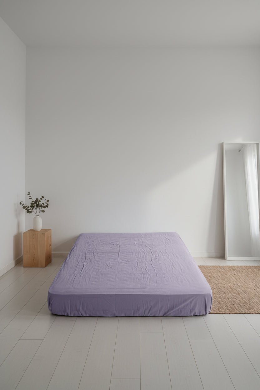 Violet stonewashed cotton fitted sheet styled on a bed, showing soft muted purple tone, relaxed texture and secure fitted design.