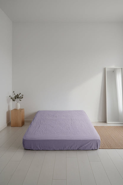 Violet stonewashed cotton fitted sheet styled on a bed, showing soft muted purple tone, relaxed texture and secure fitted design.