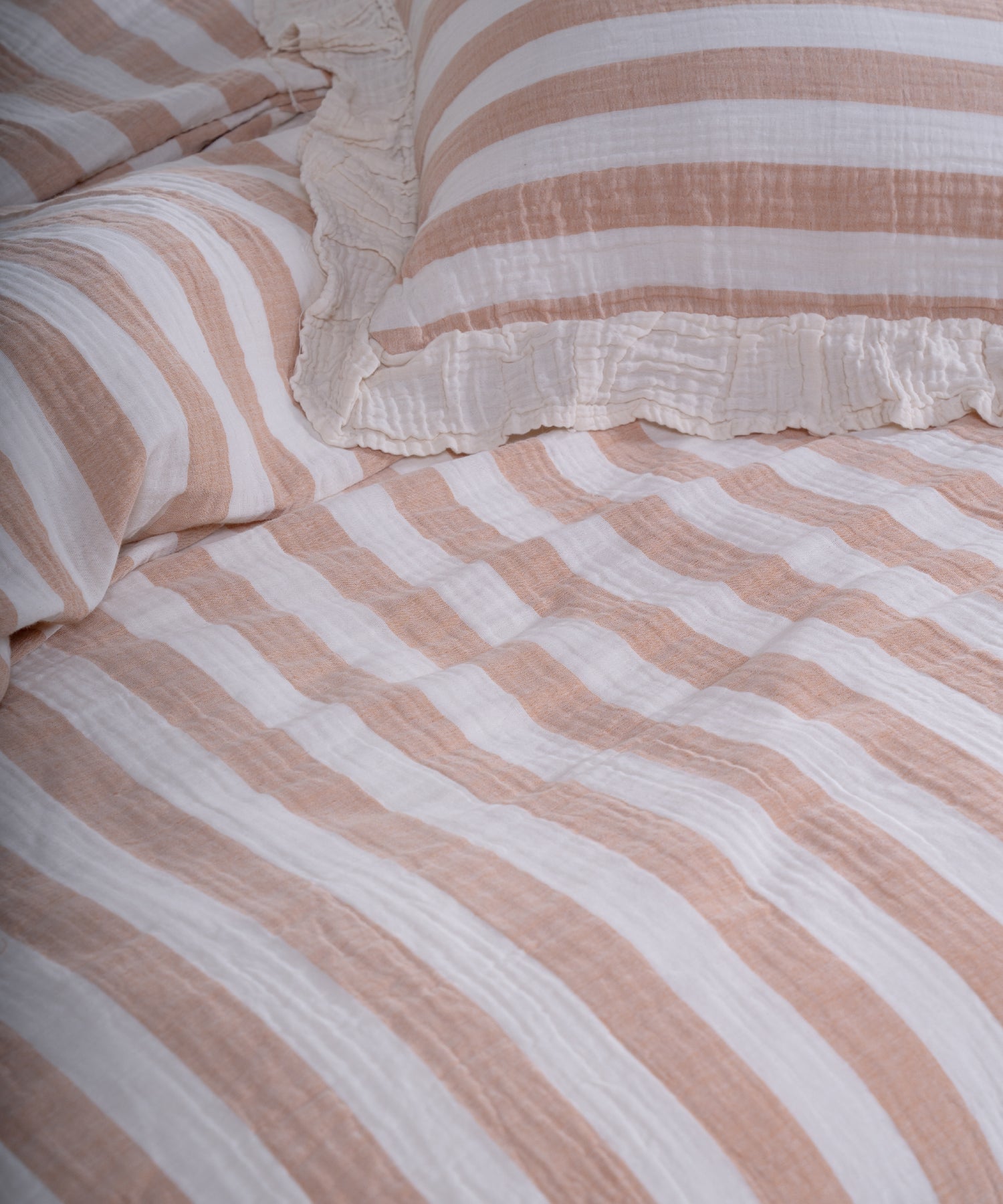 Close-up of yarn dyed 100% cotton muslin fabric with garment washed finish, natural cream base with beige and mustard stripes