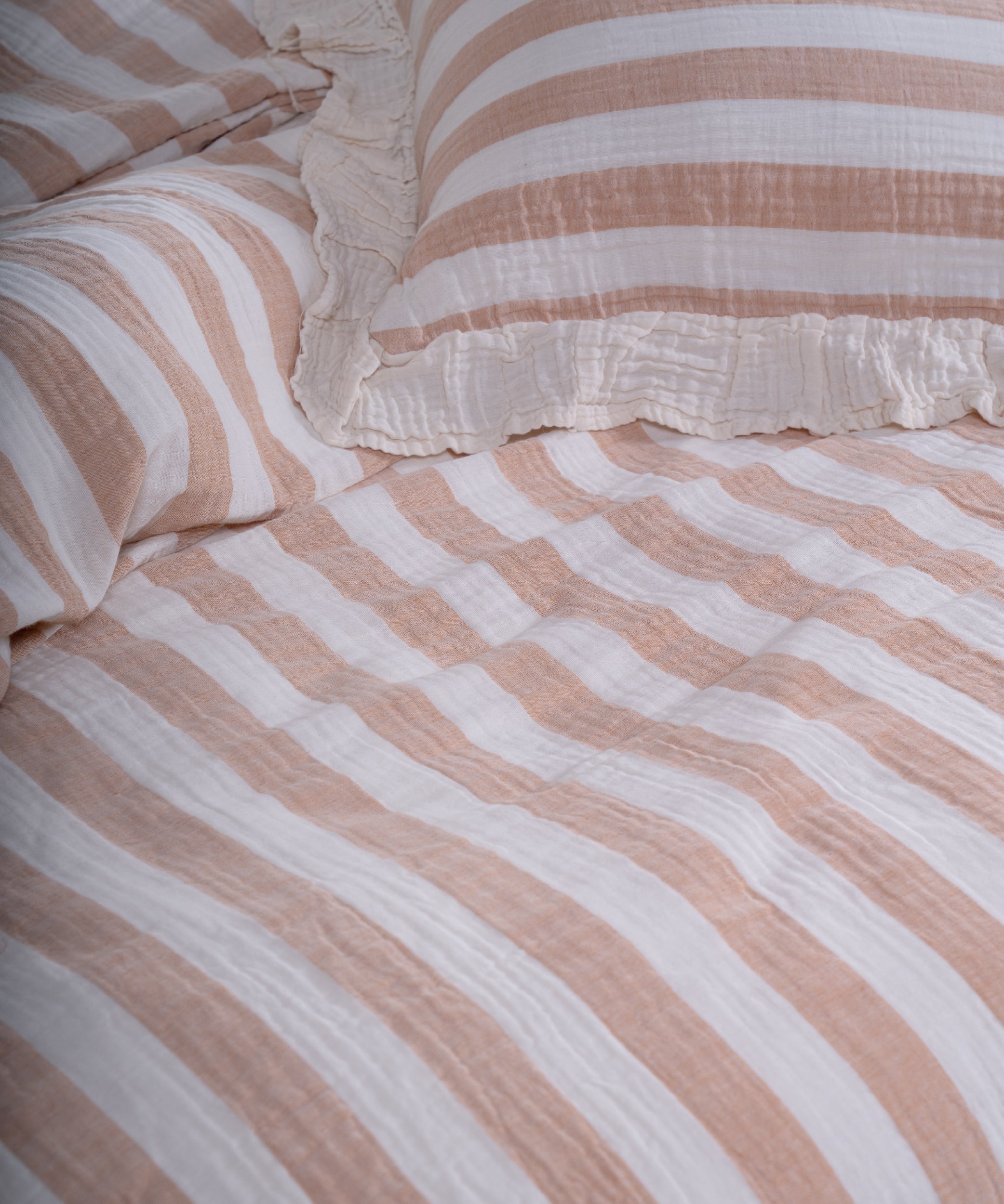 Close-up of yarn dyed 100% cotton muslin fabric with garment washed finish, natural cream base with beige and mustard stripes