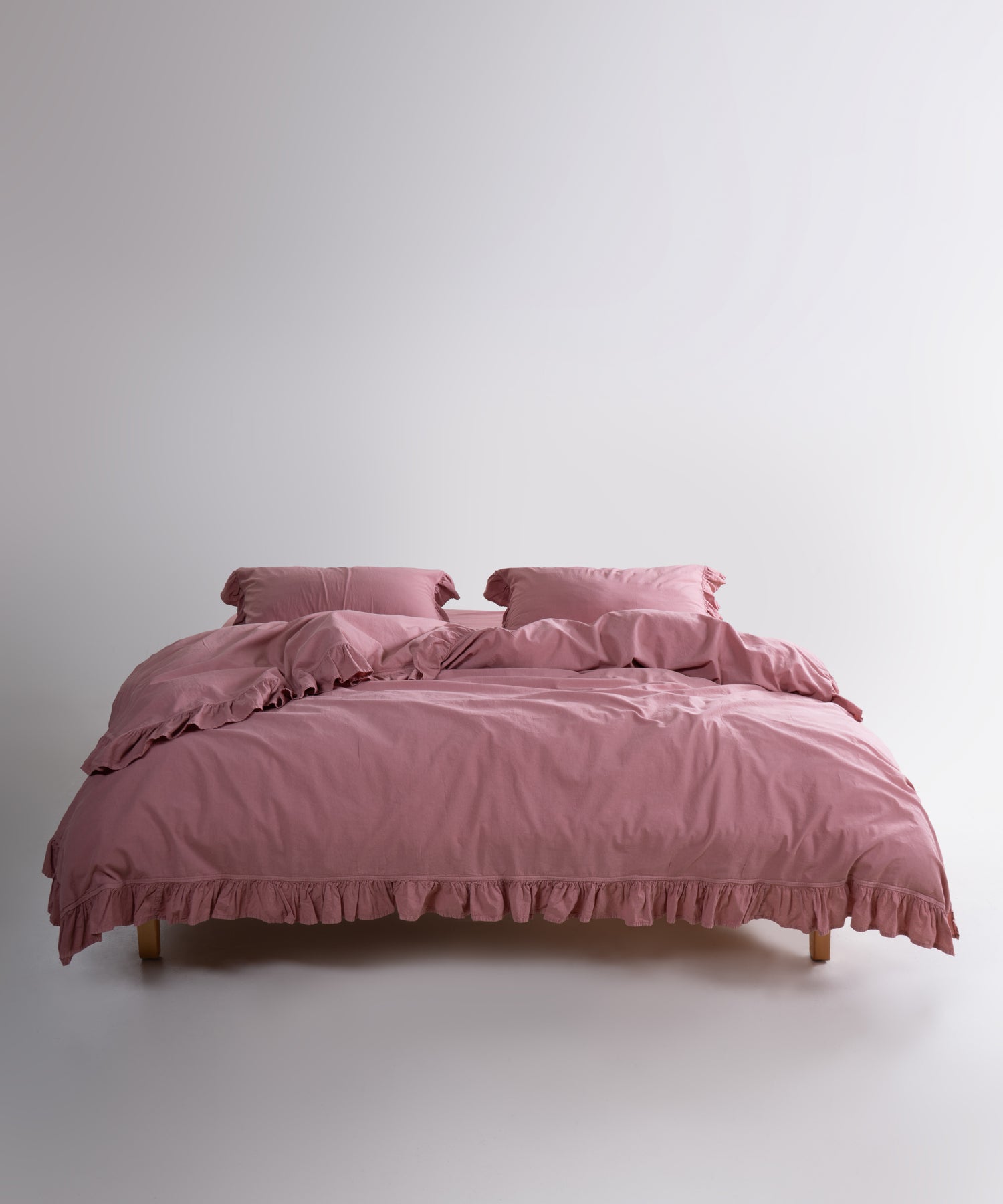 Old rose stonewashed cotton duvet cover set displayed on bed with ruffled edges and soft texture