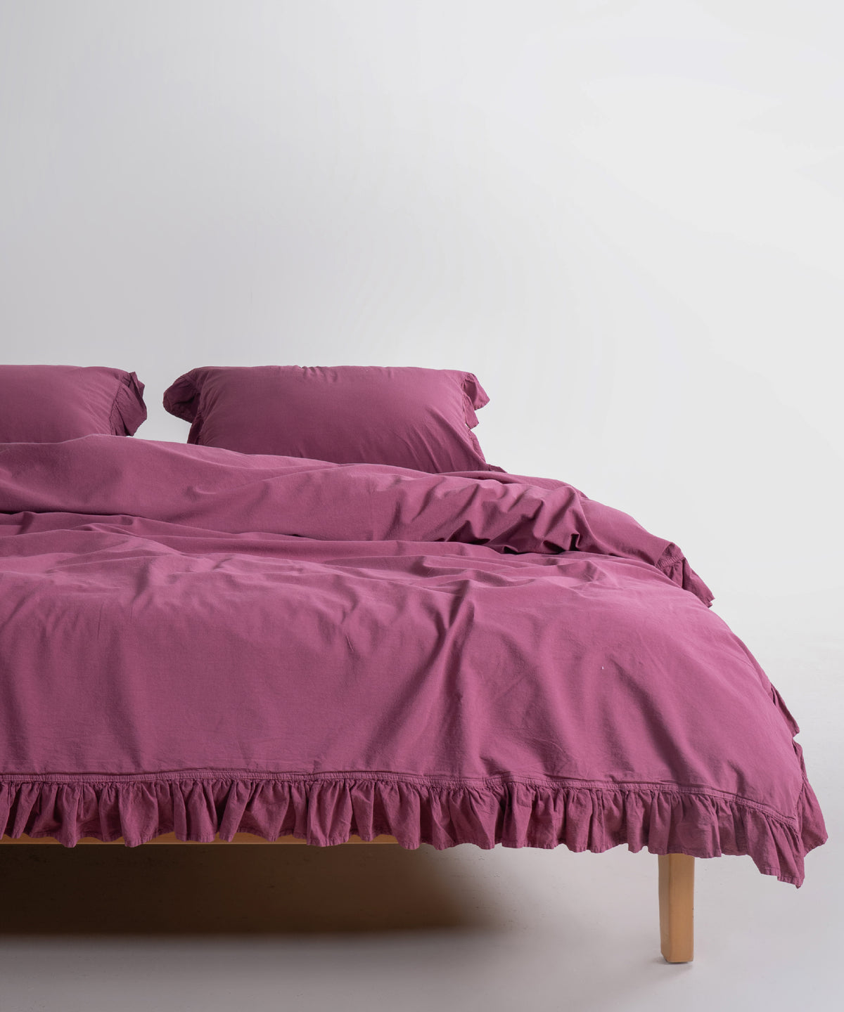 Stonewashed Exclusive Ruffled Duvet Cover Set Raspberry on a double bed with matching pillowcases – Limasso London