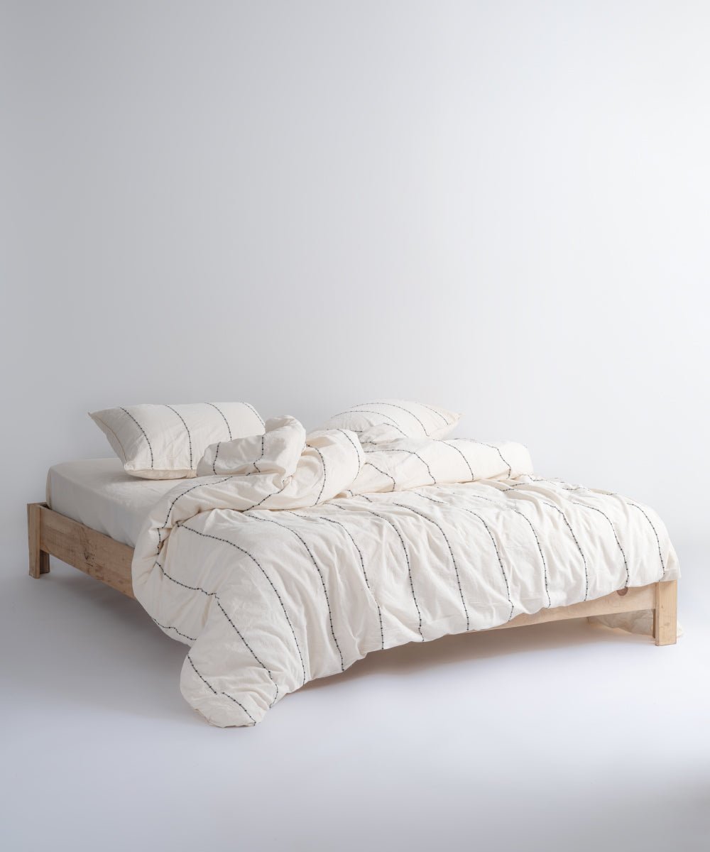Garmenwashed Vilnuss 100% cotton duvet cover set in natural cream with black dotted stripes on a wooden bed frame